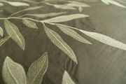 Nahaufnahme von Bettwäsche mit gesticktem Blattmuster in Grün- und Beigetönen, von oben betrachtet.