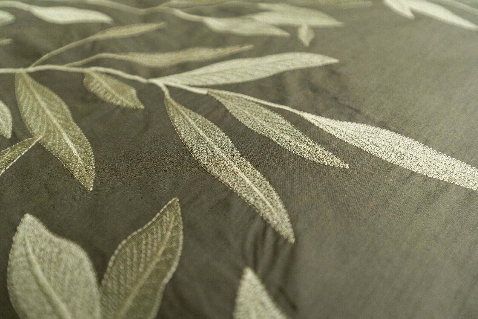 Nahaufnahme von Bettwäsche mit gesticktem Blattmuster in Grün- und Beigetönen, von oben betrachtet.