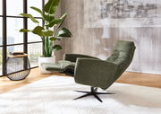 Grüner Relax-Sessel in seitlicher Perspektive, neben einem Beistelltisch und einer großen Zimmerpflanze, in einem modernen Wohnzimmer mit großen Fenstern.