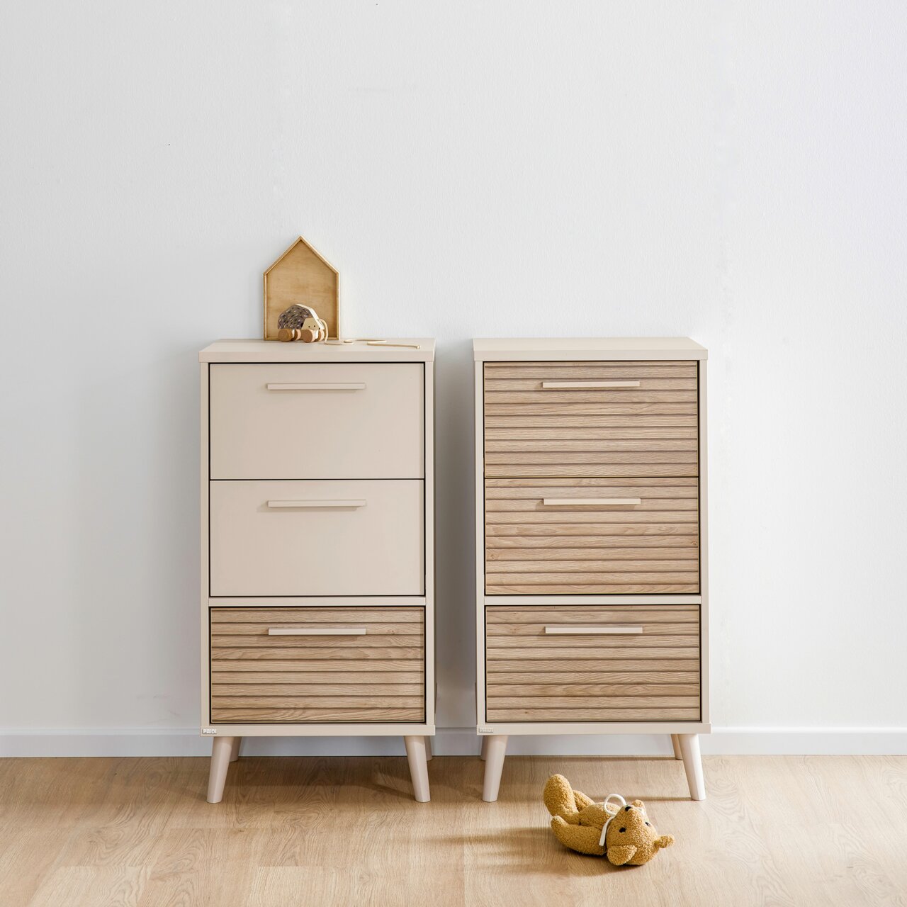 Twee moderne ladekasten van licht hout en beige, gefotografeerd van voren, op een houten vloer, met een klein decoratiestuk en een knuffel ernaast.