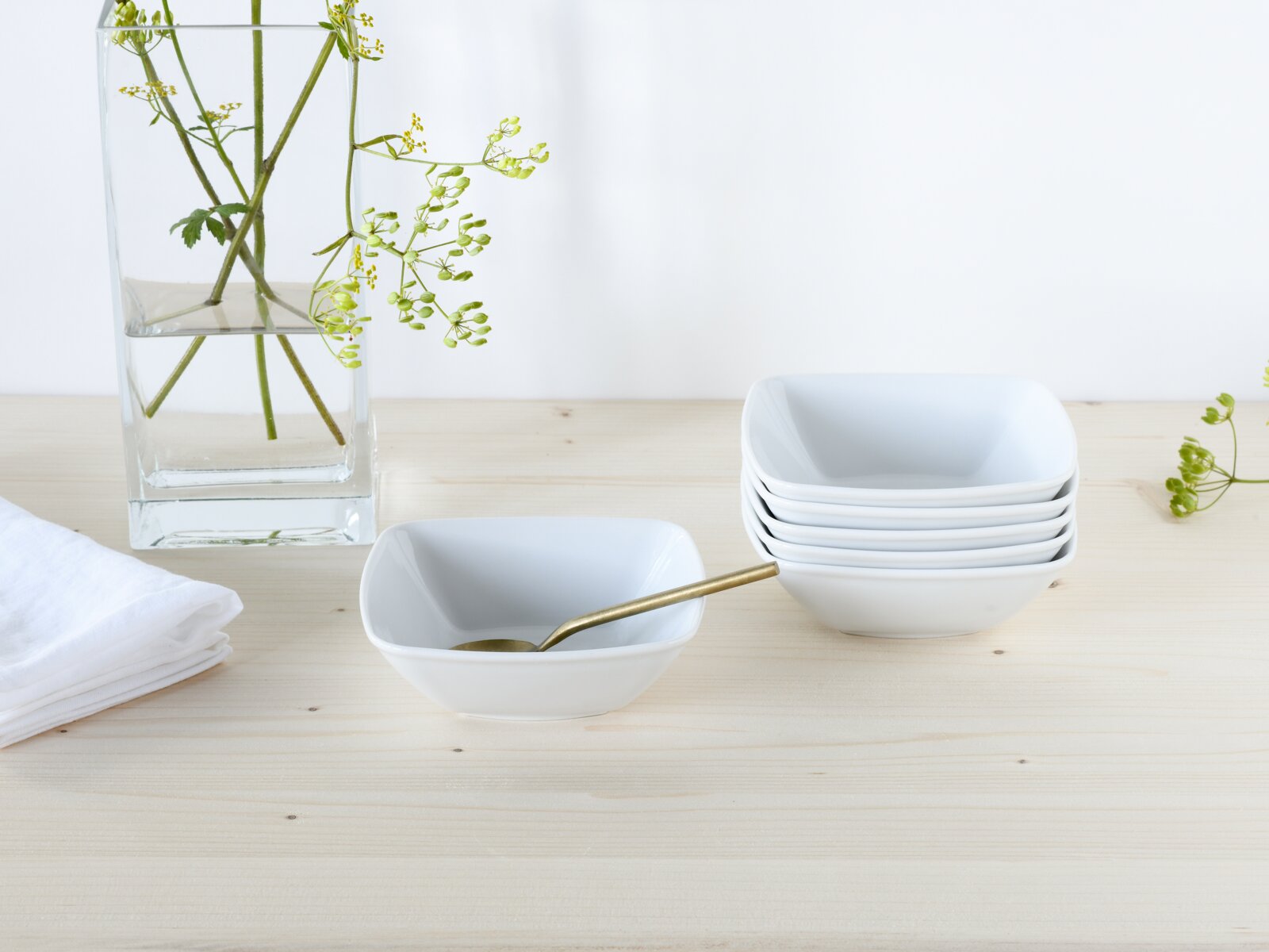 Creatable Müslischalen 6-tlg VICTORIA Weiße, quadratische Porzellanschalen (ein Stapel und eine einzelne mit goldenem Löffel) auf hellem Holztisch, links Glasvase mit grünen Zweigen; Frontansicht leicht von oben