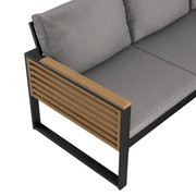 Detailansicht eines Lounge-Sets mit grauen Kissen und Holzarmlehne, seitliche Perspektive