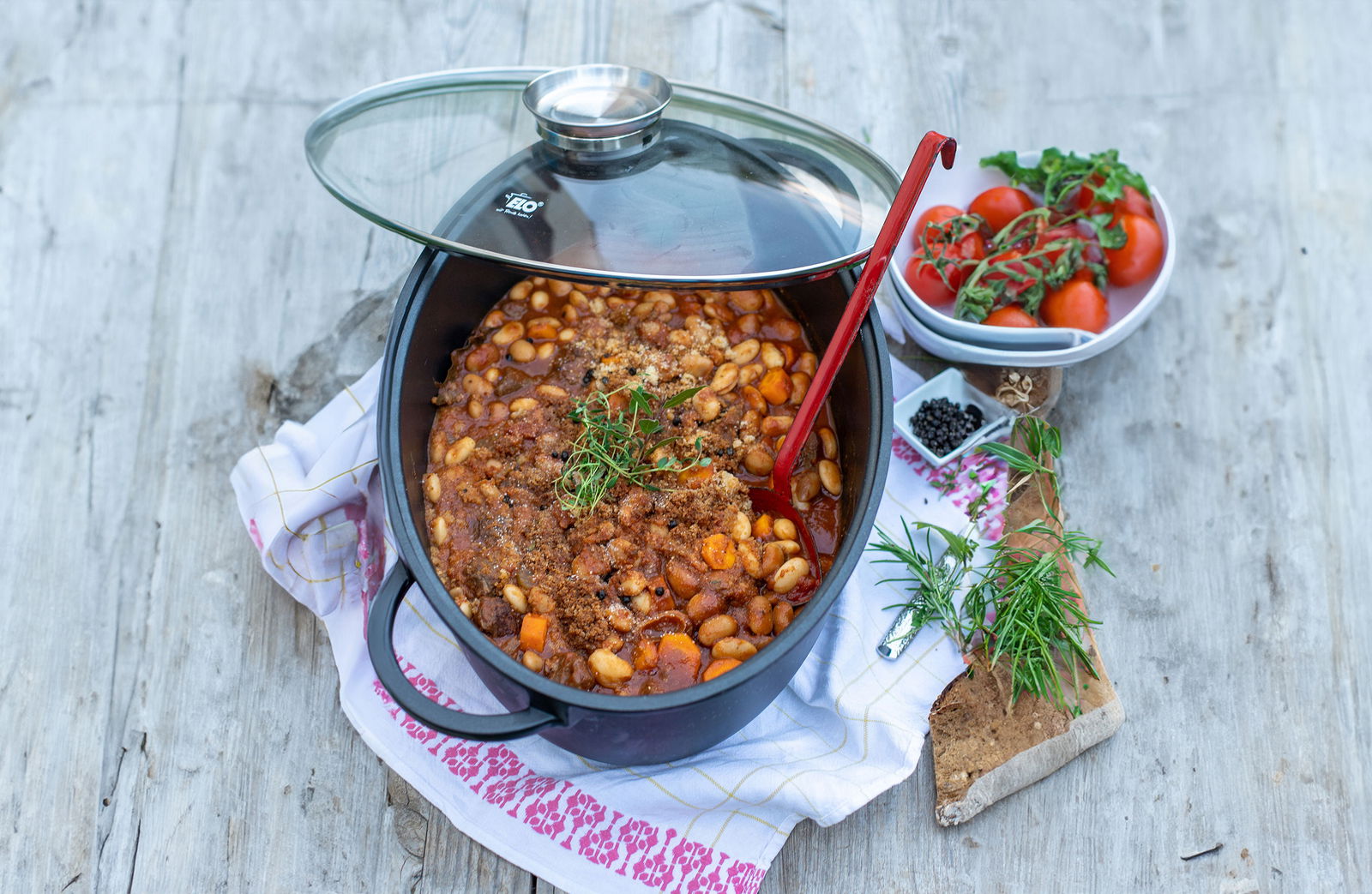 ELO Alucast Bräter oval ELODUR mit Glasdeckel, gefüllt mit einem Eintopf aus Bohnen und Gemüse, von oben fotografiert.