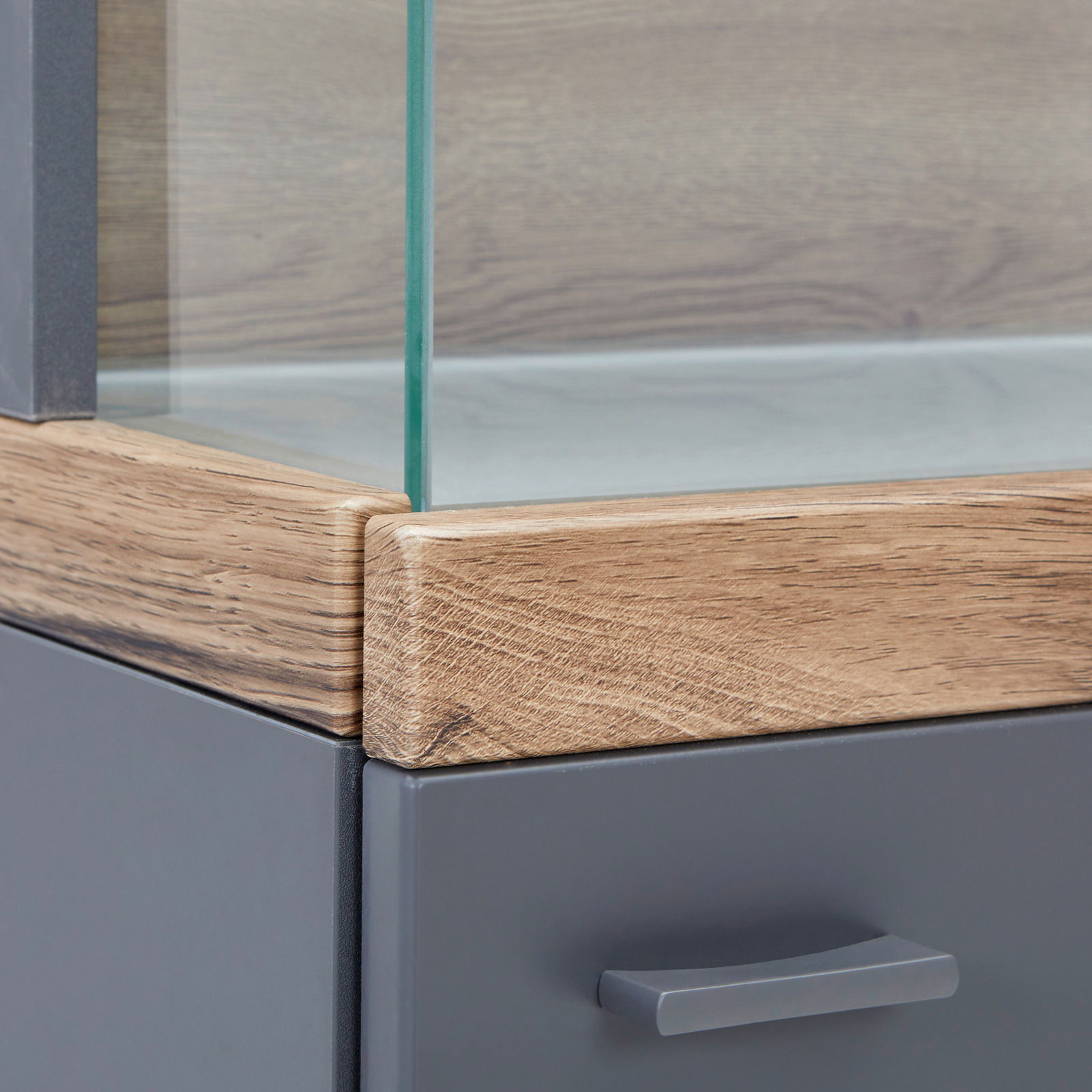 Nahaufnahme einer Vitrine mit Glasausschnitt, Holzrahmen und grauer Schublade, Perspektive von der Ecke.