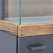 Nahaufnahme einer Vitrine mit Glasausschnitt, Holzrahmen und grauer Schublade, Perspektive von der Ecke.