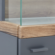 Nahaufnahme einer Vitrine mit Glasausschnitt, Holzrahmen und grauer Schublade, Perspektive von der Ecke.