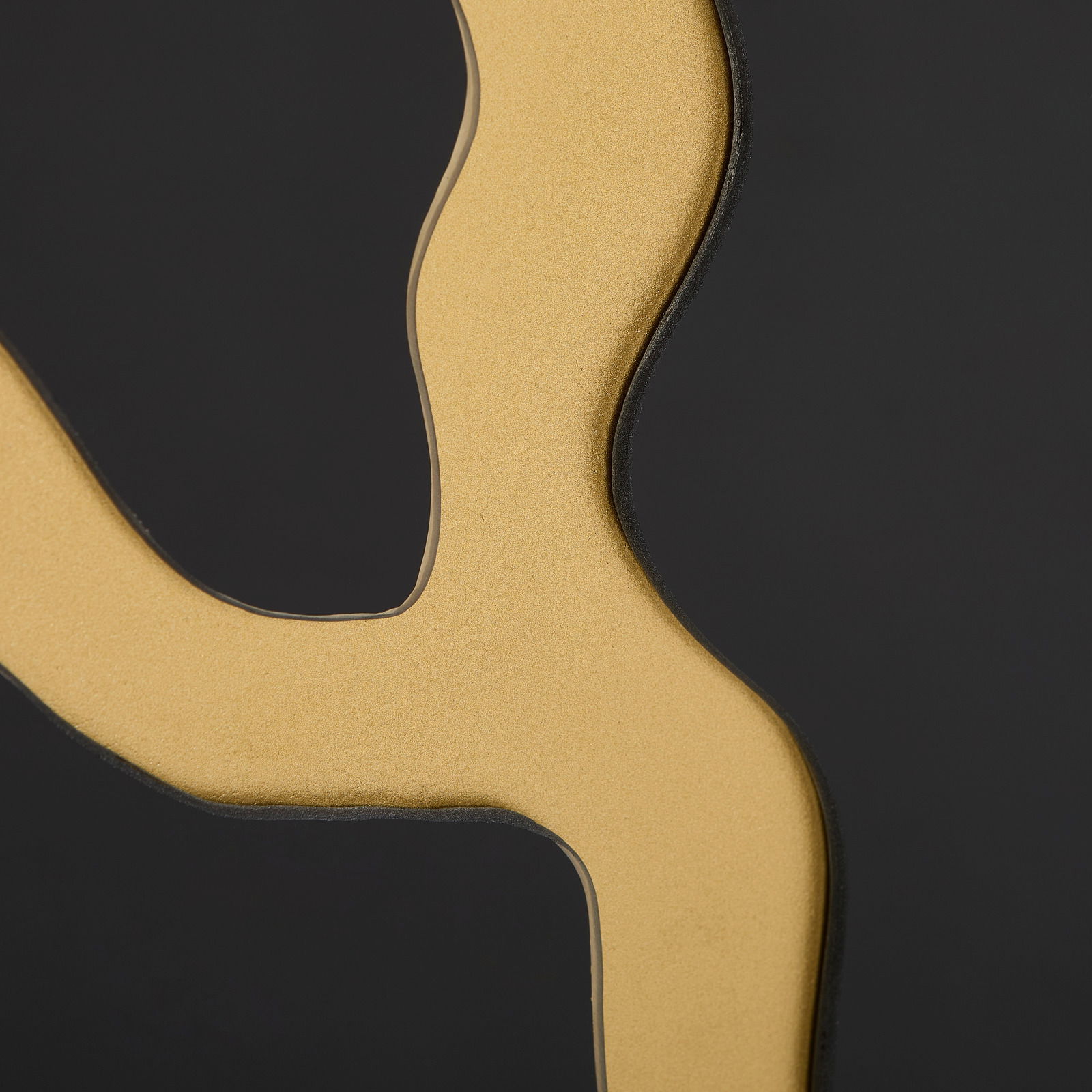 Nahaufnahme eines goldenen, geschwungenen Details auf schwarzem Hintergrund, perspektivisch von der Seite betrachtet.