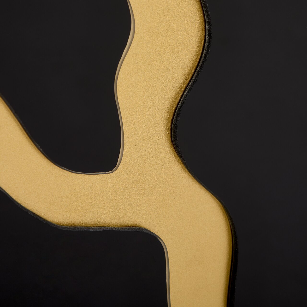 Nahaufnahme eines goldenen, geschwungenen Details auf schwarzem Hintergrund, perspektivisch von der Seite betrachtet.