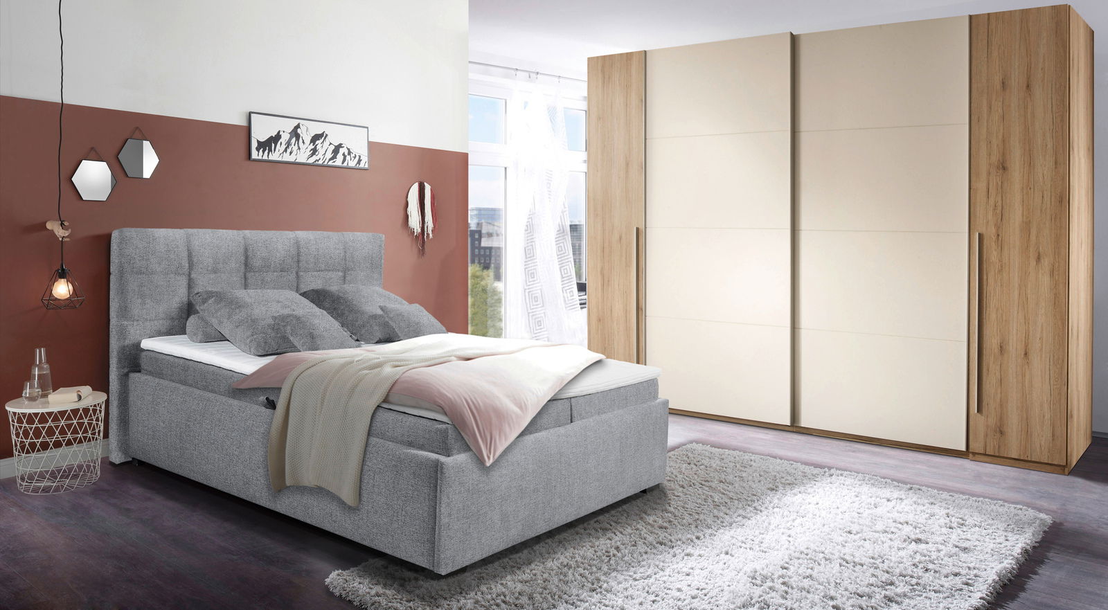 Graues Polsterbett mit hohem Kopfteil, dekoriert mit Kissen und Decke, in einem modernen Schlafzimmer mit Teppich und großem Kleiderschrank, seitliche Perspektive.