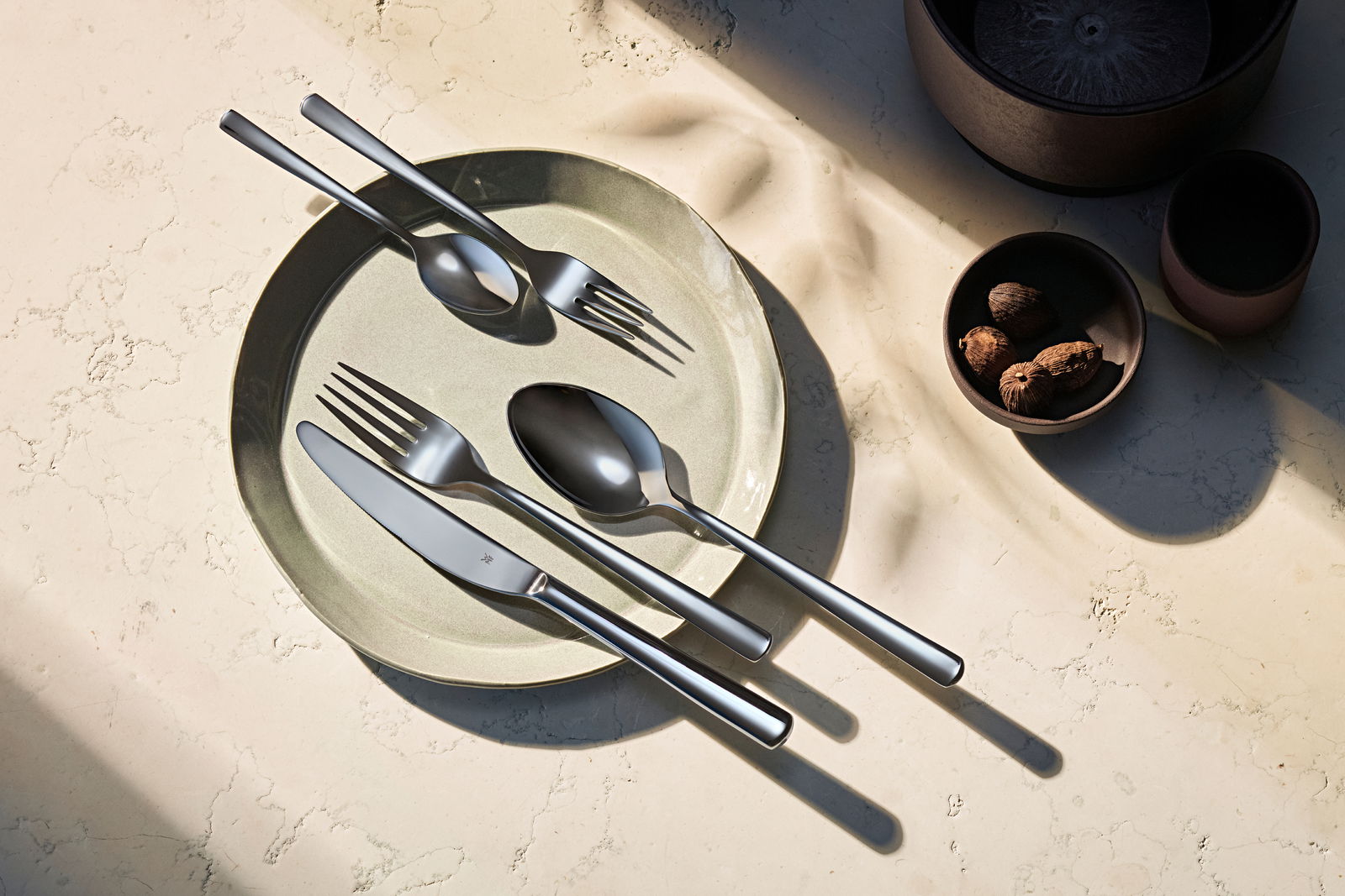 Elegantes Besteckset Philadelphia 60-tlg. auf einem Teller, von oben fotografiert, mit natürlichem Licht und Schatteneffekten.