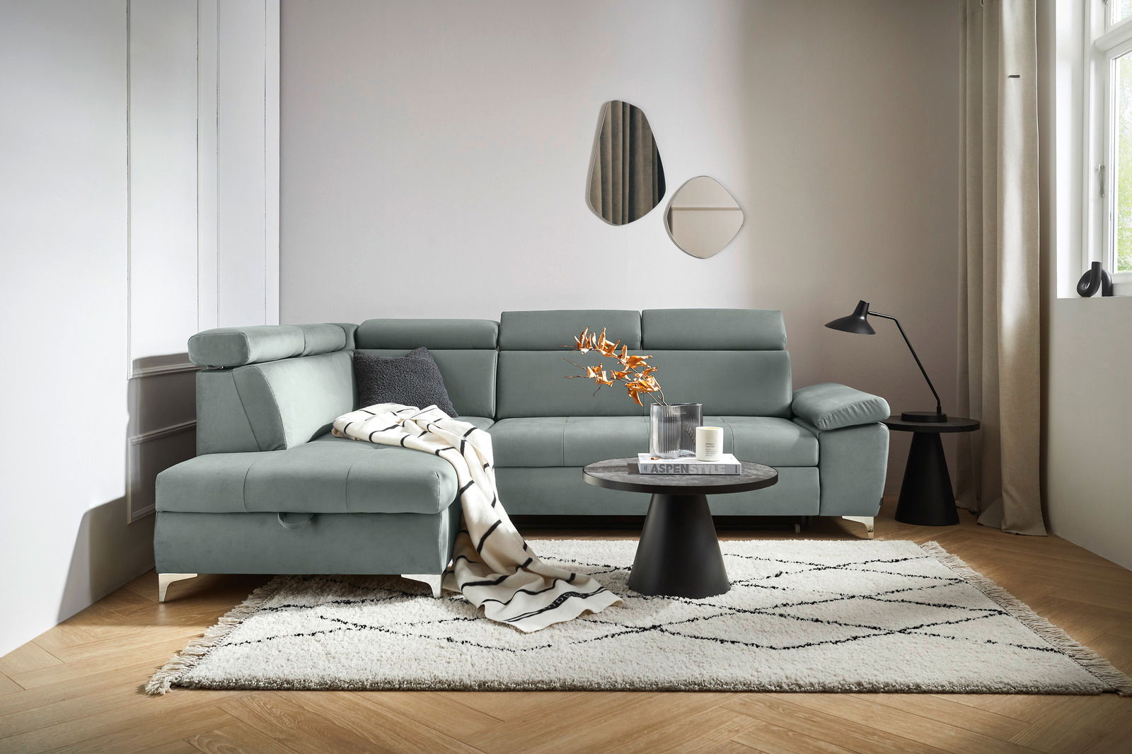 Moderne Rundecke in L-Form in einem hellen Wohnzimmer, mit einem grauen Stoffbezug und verstellbaren Kopfstützen, von vorne betrachtet.