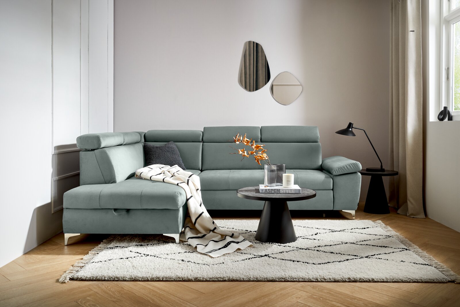 Moderne Rundecke in L-Form in einem hellen Wohnzimmer, mit einem grauen Stoffbezug und verstellbaren Kopfstützen, von vorne betrachtet.