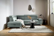 Moderne Rundecke in L-Form in einem hellen Wohnzimmer, mit einem grauen Stoffbezug und verstellbaren Kopfstützen, von vorne betrachtet.