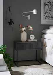 Moderne Nachtkommode in dunklem Design mit dekorativer Vase und Uhr, seitliche Perspektive