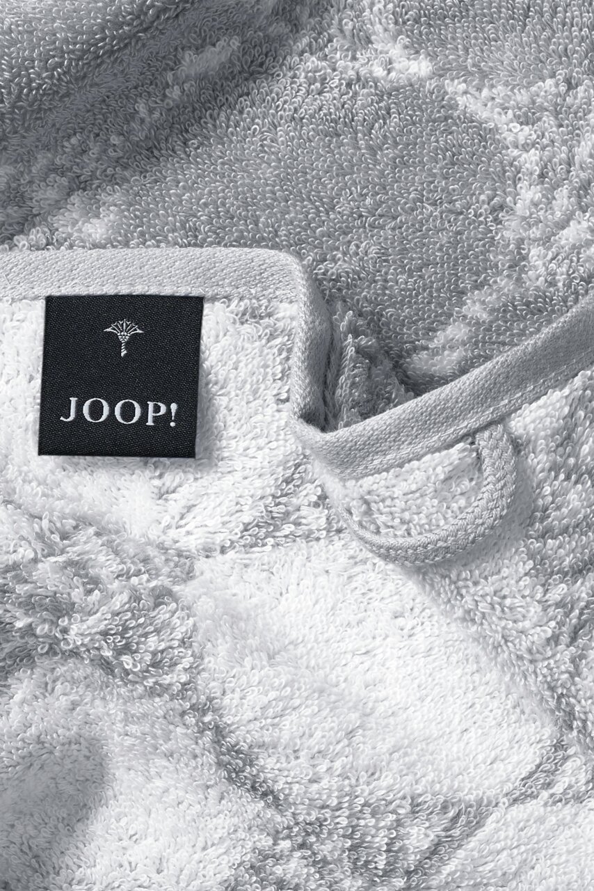 Close-up van een zachte, grijze gastendoek met een zwart label waarop 'JOOP!' staat.