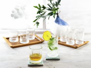 Ein Set aus Longdrinkbechern Elysia, präsentiert auf einem Tisch mit dekorativen Untersetzern und einem frischen Getränk mit Zitrone und Minze, aus einer seitlichen Perspektive fotografiert.