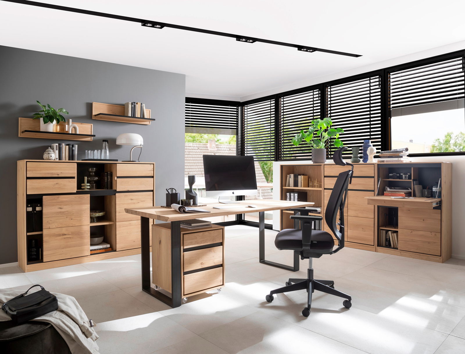 Moderne Büroumgebung mit einem großen Schreibtisch aus Holz in der Mitte, umgeben von Regalen und Schränken aus hellem Holz. Die Perspektive zeigt den Raum von vorne mit Blick auf den Schreibtisch und die umgebenden Möbel.