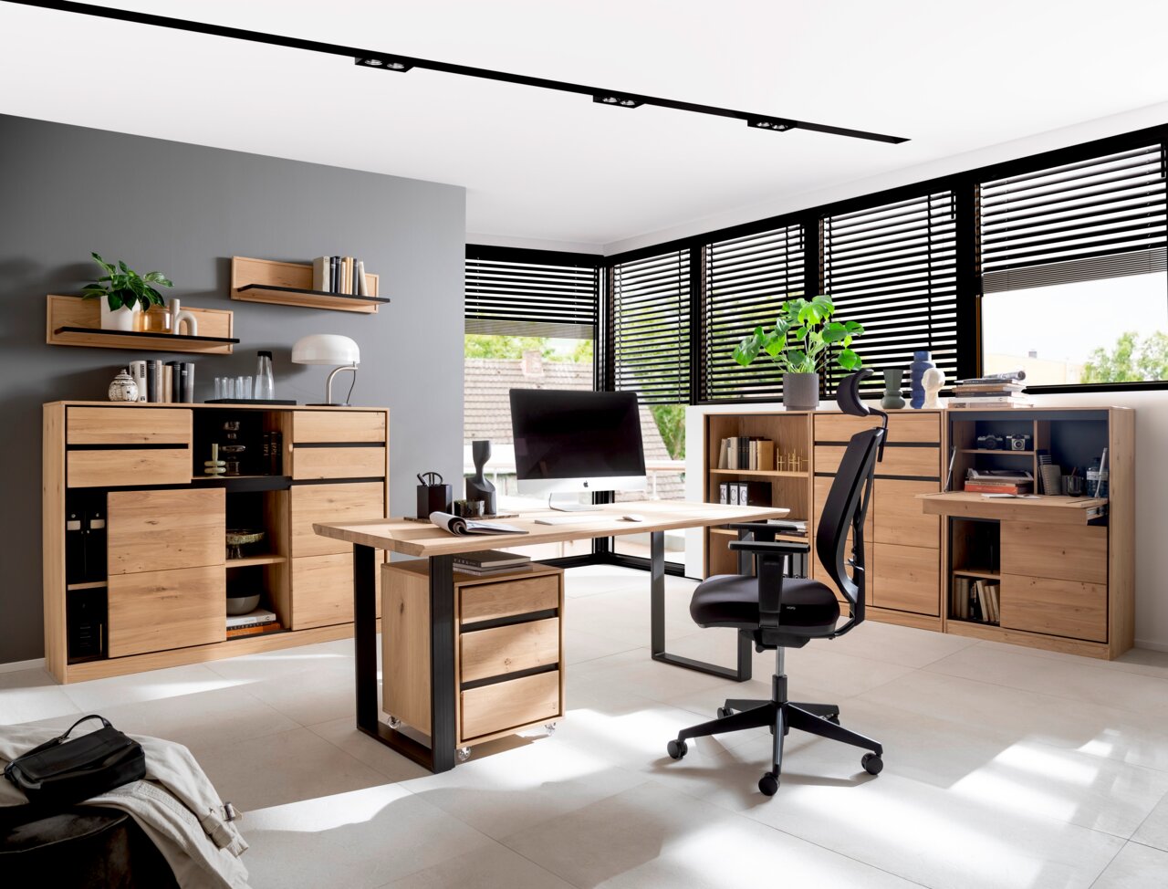 Moderne Büroumgebung mit einem großen Schreibtisch aus Holz in der Mitte, umgeben von Regalen und Schränken aus hellem Holz. Die Perspektive zeigt den Raum von vorne mit Blick auf den Schreibtisch und die umgebenden Möbel.