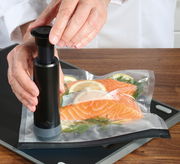 Vakuumier-Set EASYFRESH in Benutzung, Nahaufnahme von oben, zeigt Hände, die eine Vakuumpumpe auf einem Beutel mit Lachs und Zitronenscheiben bedienen.