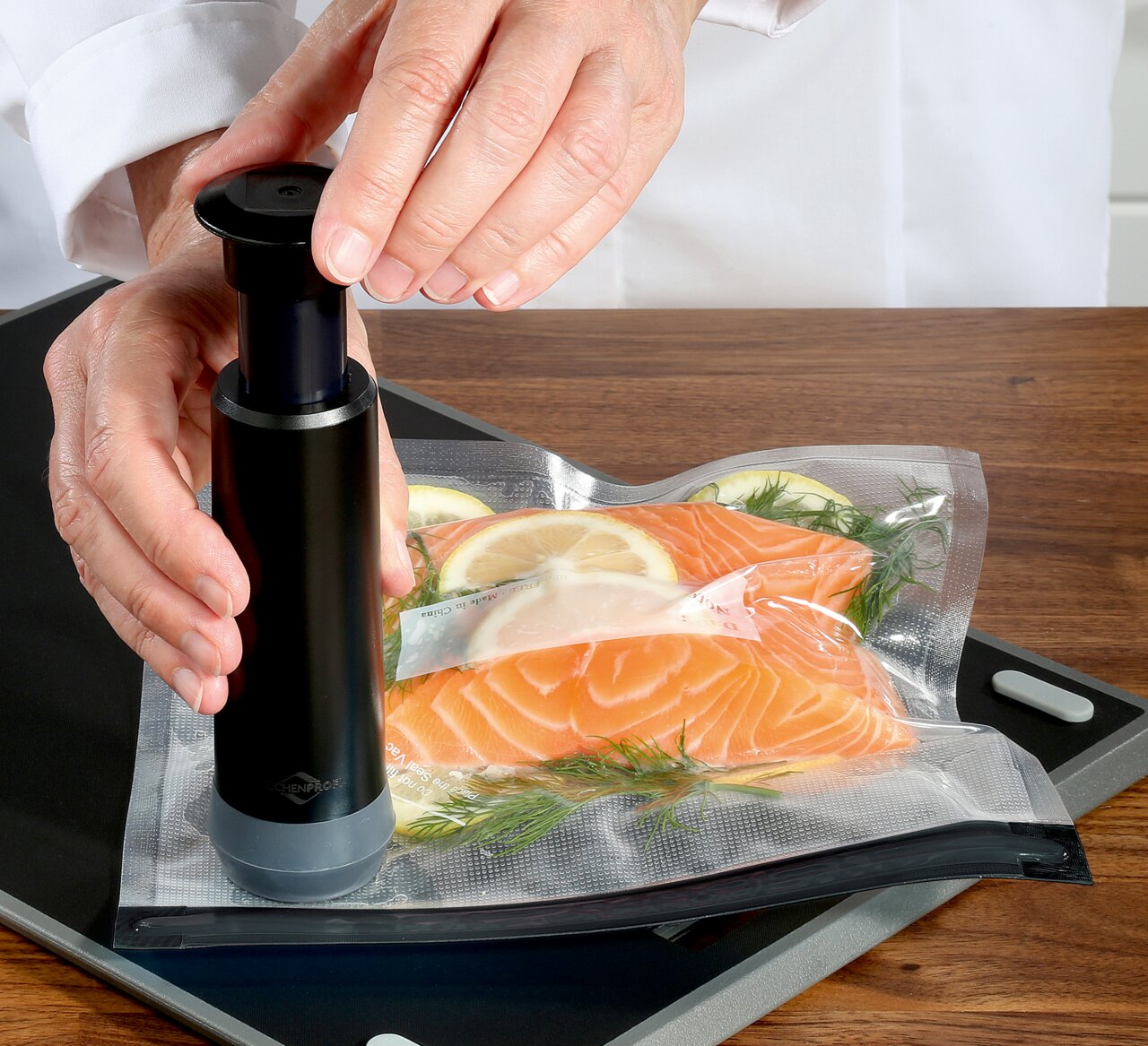 Vakuumier-Set EASYFRESH in Benutzung, Nahaufnahme von oben, zeigt Hände, die eine Vakuumpumpe auf einem Beutel mit Lachs und Zitronenscheiben bedienen.
