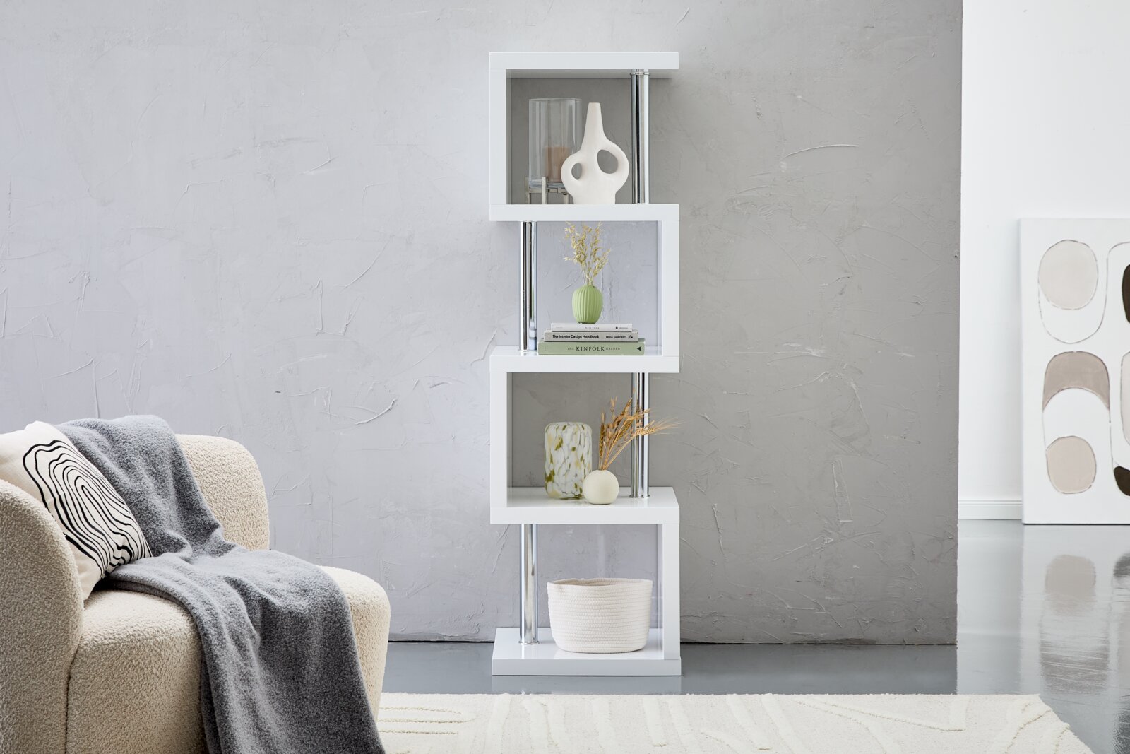 Modernes, weißes Regal mit asymmetrischem Design, dekoriert mit Vasen und Büchern, seitliche Perspektive.