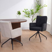 Zwei Schwingstühle in einem modernen Raum, einer in Beige und einer in Schwarz, mit einem Holztisch und Pflanzen im Hintergrund, seitliche Perspektive.