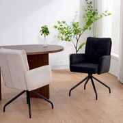 Zwei Schwingstühle in einem modernen Raum, einer in Beige und einer in Schwarz, mit einem Holztisch und Pflanzen im Hintergrund, seitliche Perspektive.