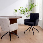Twee schommelstoelen in een moderne ruimte, één in beige en één in zwart, met een houten tafel en planten op de achtergrond, gezien vanuit de zijkant.