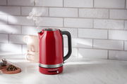 Roter Wasserkocher mit 1,7 Liter Fassungsvermögen, seitliche Perspektive, auf einer Küchenarbeitsplatte mit dampfendem Ausguss.