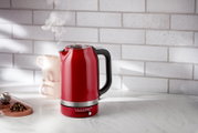 Roter Wasserkocher mit 1,7 Liter Fassungsvermögen, seitliche Perspektive, auf einer Küchenarbeitsplatte mit dampfendem Ausguss.