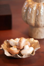 Goldene Schale mit gewelltem Rand, gefüllt mit frischen Champignons, auf einem Holztisch aus der Seitenperspektive.