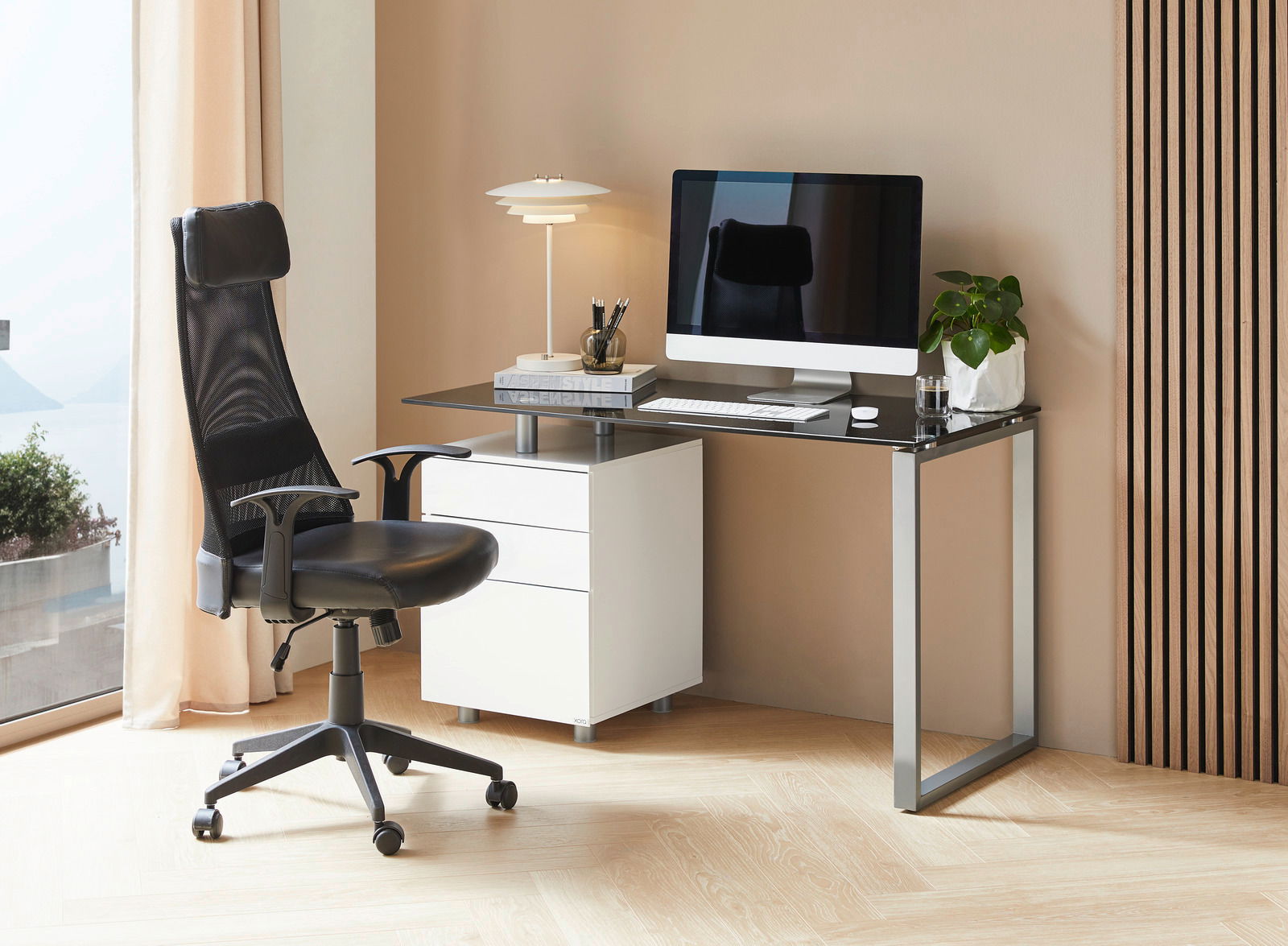 Moderner Schreibtisch mit schwarzer Glasplatte, weißem Rollcontainer und ergonomischem Bürostuhl, seitliche Perspektive.