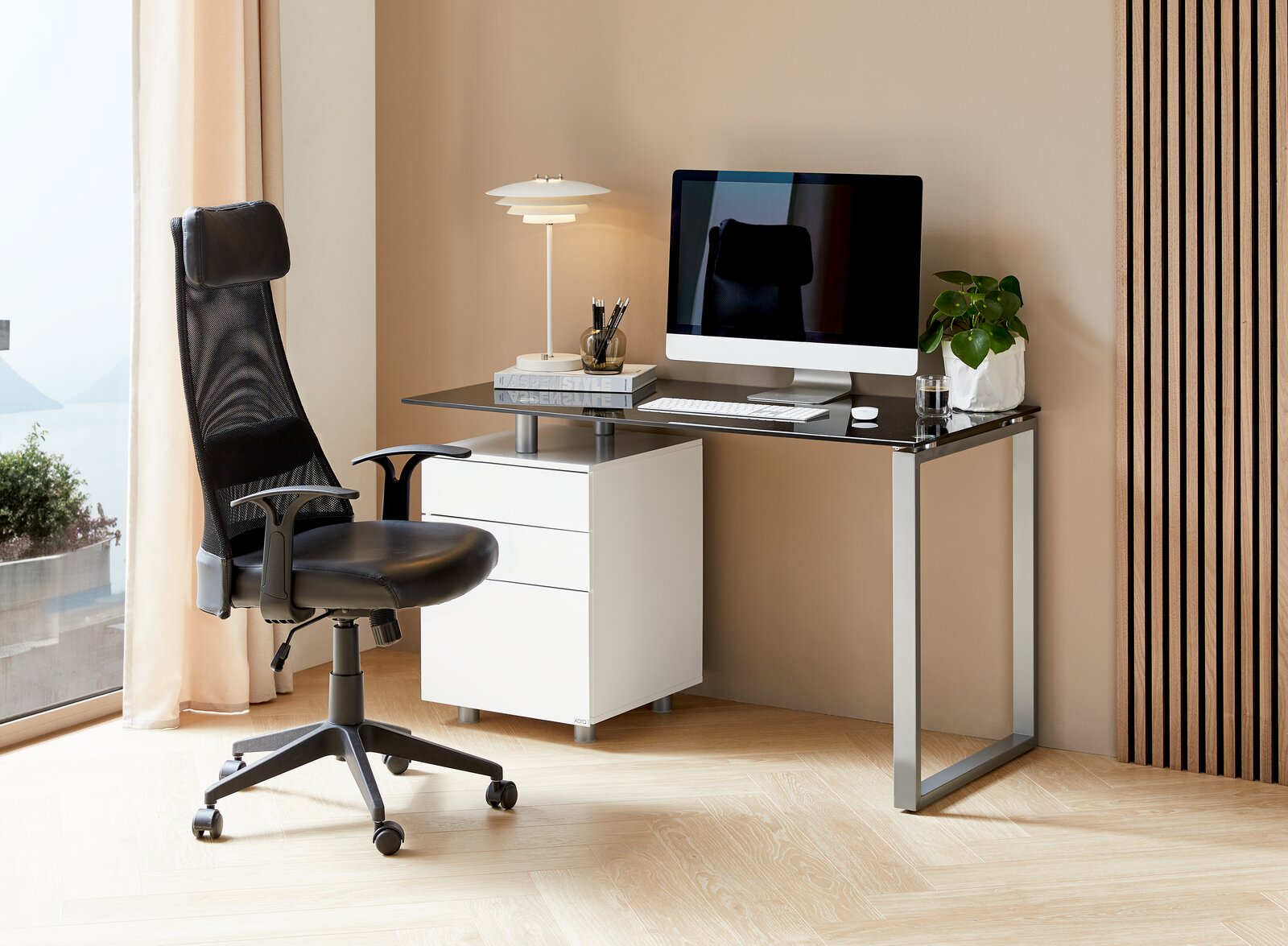 Moderner Schreibtisch mit schwarzer Glasplatte, weißem Rollcontainer und ergonomischem Bürostuhl, seitliche Perspektive.