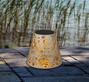 Dekorative Solarleuchte mit floralem Muster, seitliche Perspektive, auf Steinboden vor Schilf und Wasser.