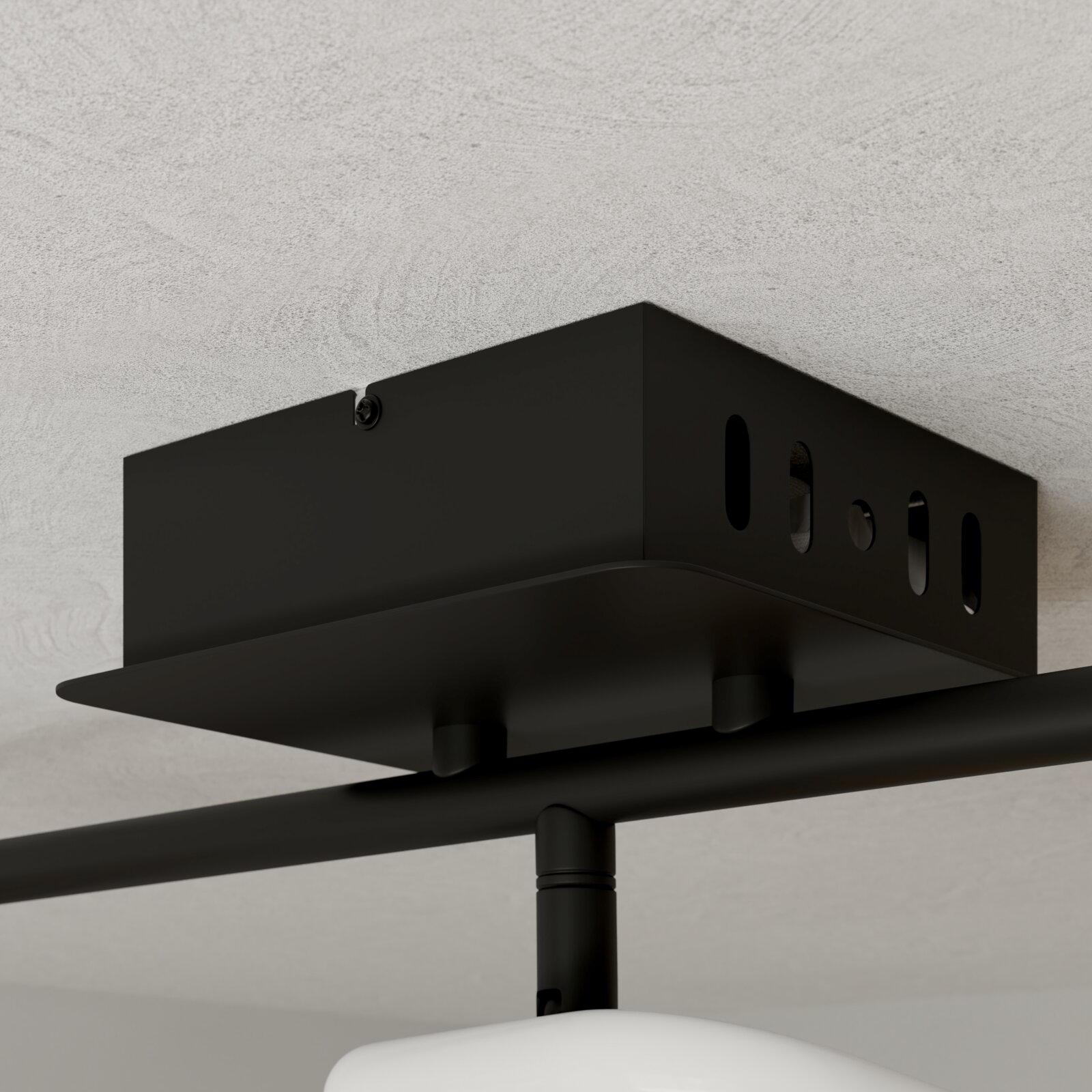 Schwarze Deckenhalterung aus Metall mit Langlöchern und Schraube, Detailansicht aus Untersicht in leichter Schrägperspektive an einer hellen Decke montiert.