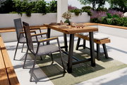 Moderner Gartentisch mit Holzplatte und Metallbeinen, umgeben von stilvollen Stühlen und einer Bank, auf einer Terrasse mit grüner Bepflanzung, aus seitlicher Perspektive fotografiert.