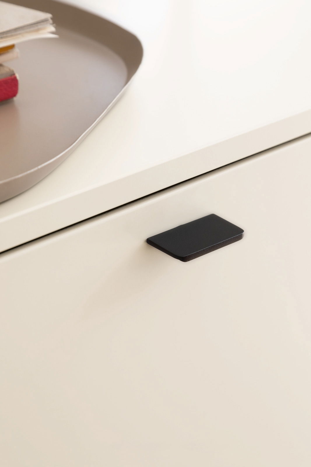 Nahaufnahme einer modernen, cremefarbenen Schublade mit schwarzem Griff, von oben betrachtet.