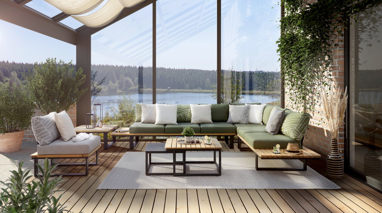 Moderne Loungeecke mit grünen und weißen Kissen auf einer Terrasse mit Blick auf einen See, umgeben von Pflanzen. Perspektive von vorne.