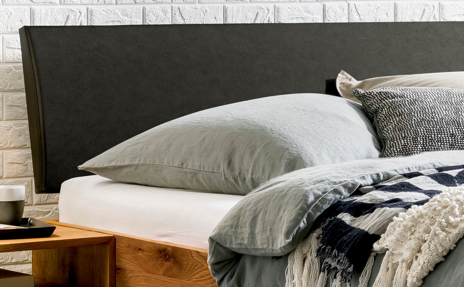 Gepolstertes Kopfteil in dunkler Farbe, seitliche Perspektive, mit Bett und Kissen im Vordergrund