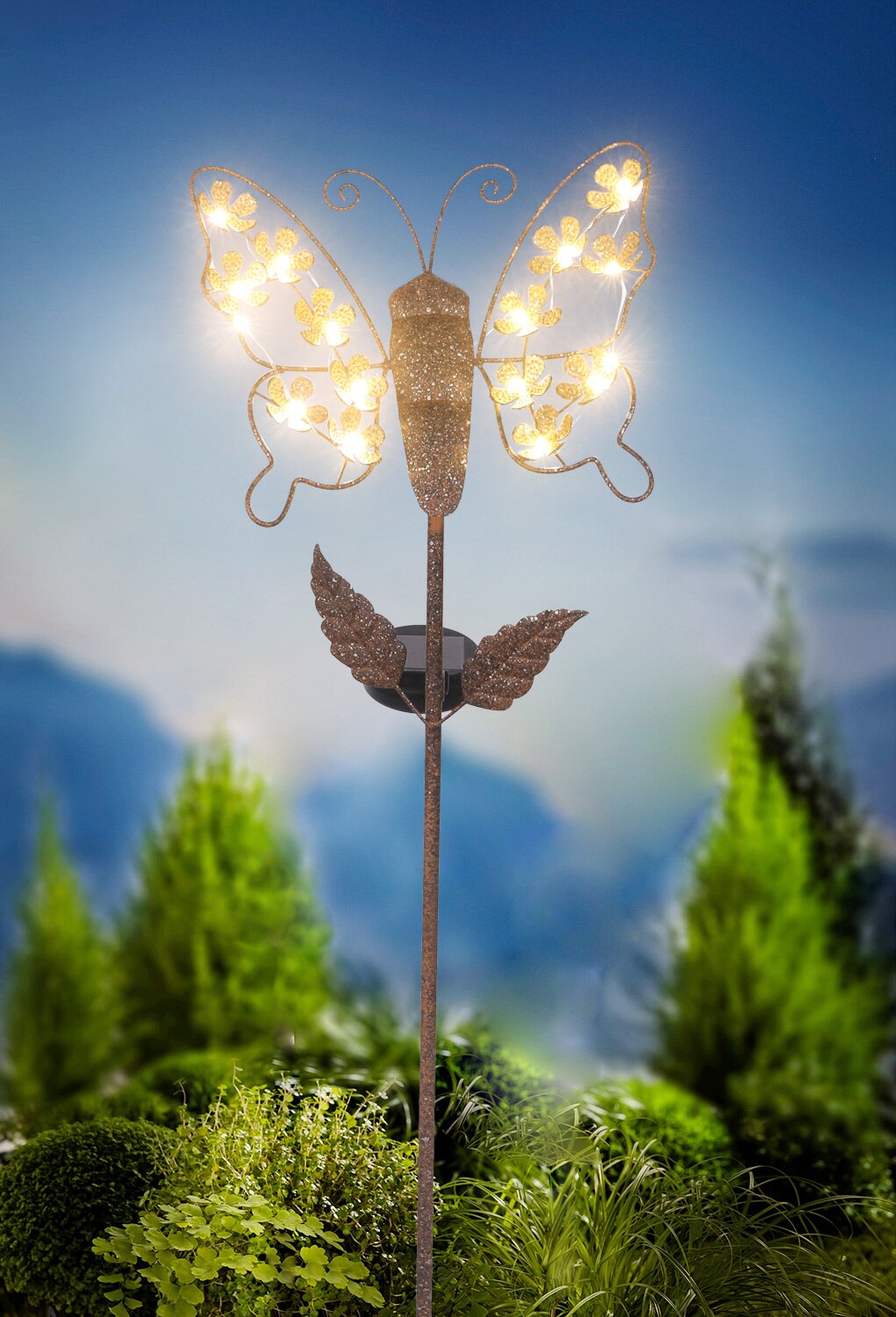 Zonne-lamp in de vorm van een vlinder met verlichte vleugels, vooraan in de tuin geplaatst.
