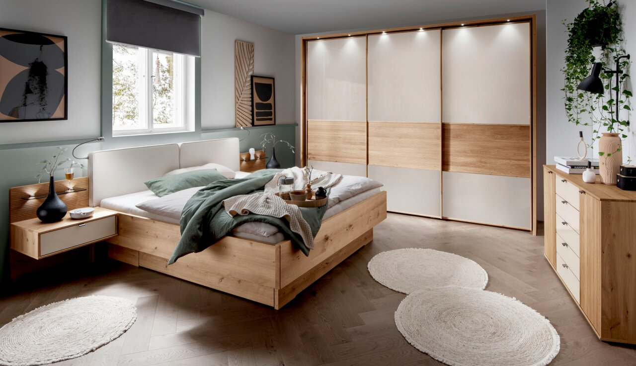 Moderner Schwebetürenschrank mit drei Türen in einem stilvollen Schlafzimmer, aus hellem Holz und weißen Paneelen, mit integrierter Beleuchtung. Perspektive: Frontalansicht.