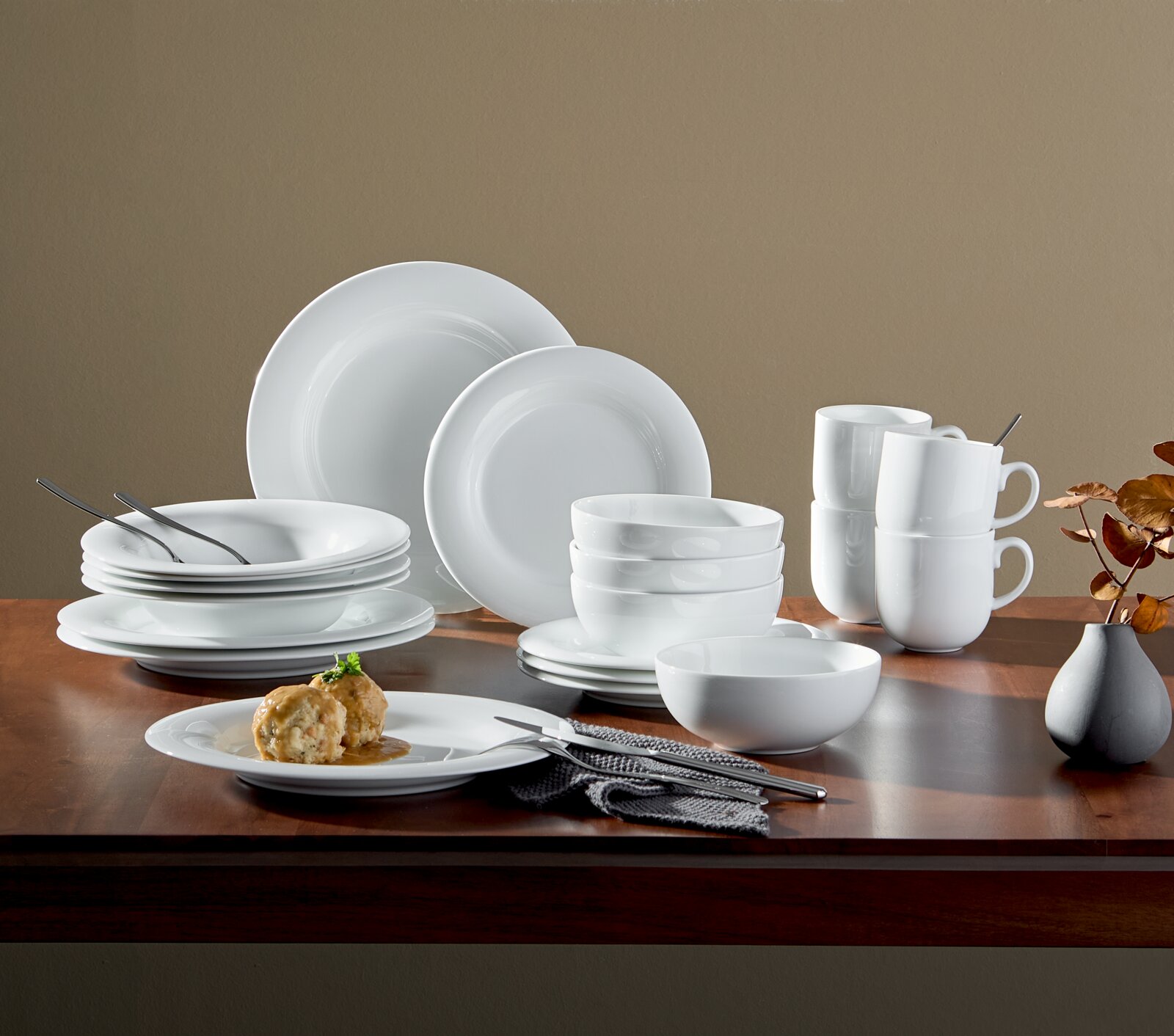 20-delig servies van wit porselein, bestaande uit borden, schalen en kopjes, opgesteld op een houten tafel, zijaanzicht.