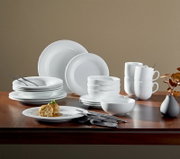 20-delig servies van wit porselein, bestaande uit borden, schalen en kopjes, opgesteld op een houten tafel, zijaanzicht.