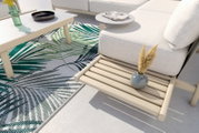Moderne Loungeeckgarnitur mit hellem Holz und beigem Polster, dekoriert mit einem kleinen Tisch, einer Vase und einem Teppich mit Blattmuster. Perspektive von oben.