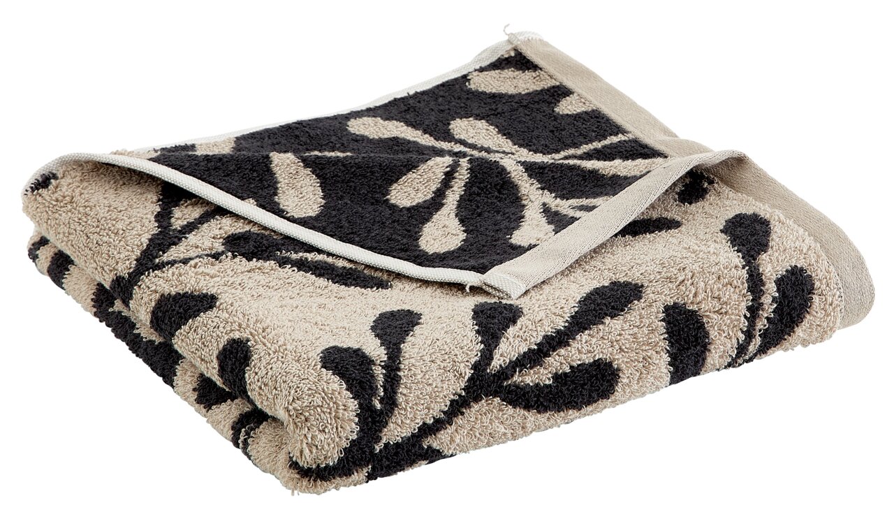 Beigefarbenes Handtuch mit schwarzem Blattmuster, gefaltet und aus seitlicher Perspektive fotografiert.