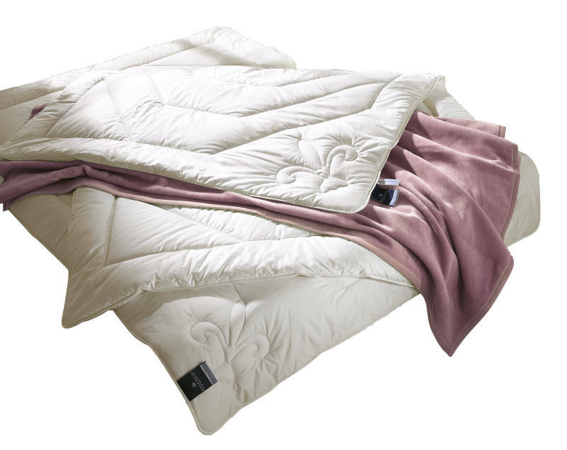 Faserdecke Uno in einer schrägen Perspektive, mit dekorativem Muster und einer lila Decke darunter.