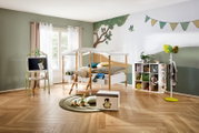 Frontalansicht eines hellen, liebevoll eingerichteten Kinderzimmers mit weißem Hausbett, Maltisch, Spielregal, Garderobe und verspielter Waldtier-Wandgestaltung.