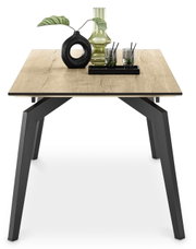 Moderne eettafel van 200 x 100 cm met houten blad en zwarte metalen poten, gefotografeerd van voren, versierd met een vaas en glazen.
