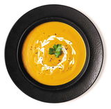 Schwarzer Teller mit Suppenschale, gefüllt mit cremiger Kürbissuppe, dekoriert mit Sahne und Petersilie, aus der Vogelperspektive.