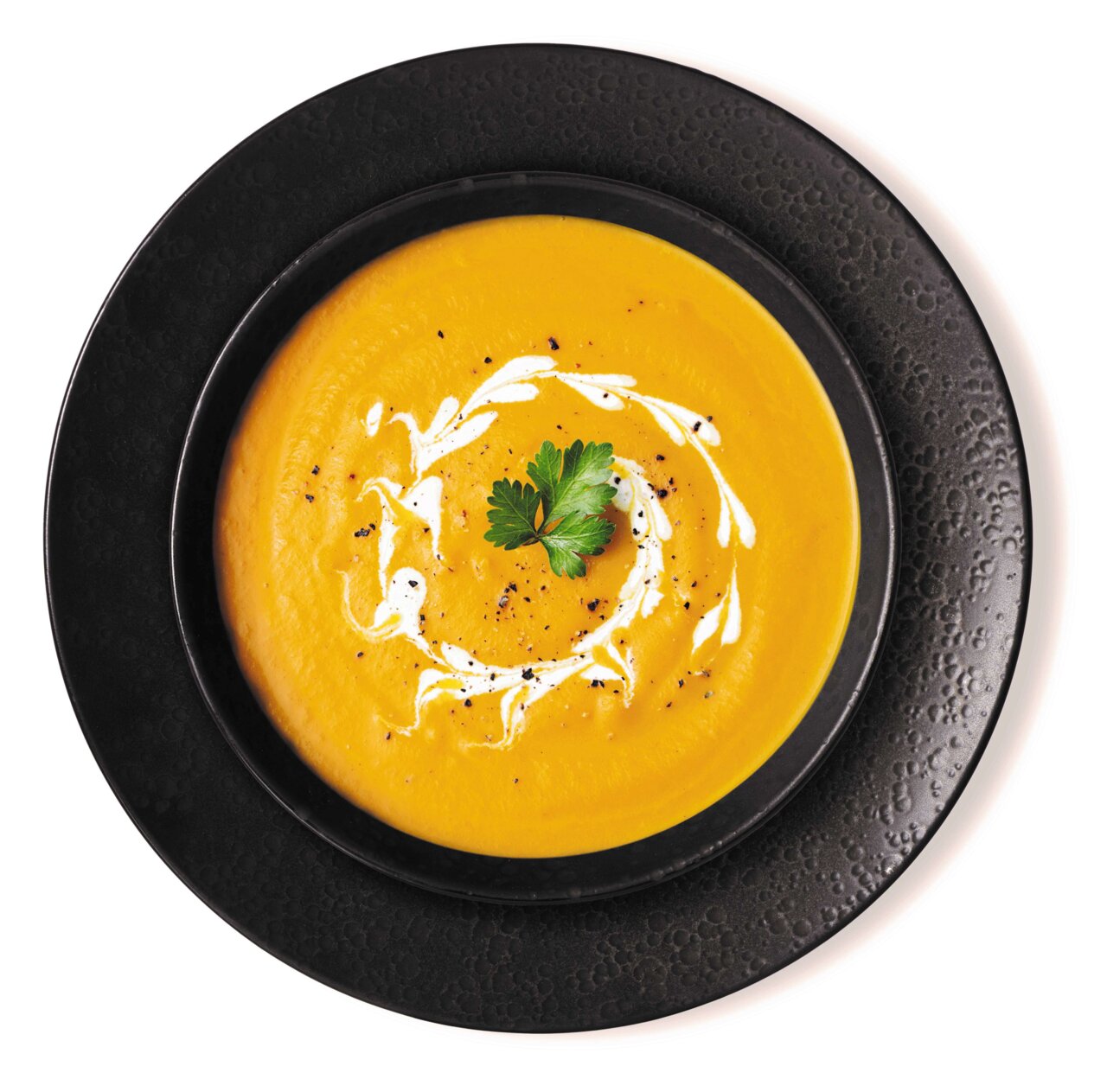 Ritzenhoff & Breker Tafelservice 8-tlg. KITWE Schwarzer Teller mit Suppenschale, gefüllt mit cremiger Kürbissuppe, dekoriert mit Sahne und Petersilie, aus der Vogelperspektive.